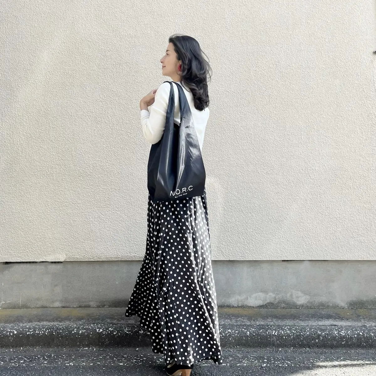 白のVネックニット、黒ベースのドット柄ロングフレアスカート、エクラ4月号付録のブラックのショッパーバッグ