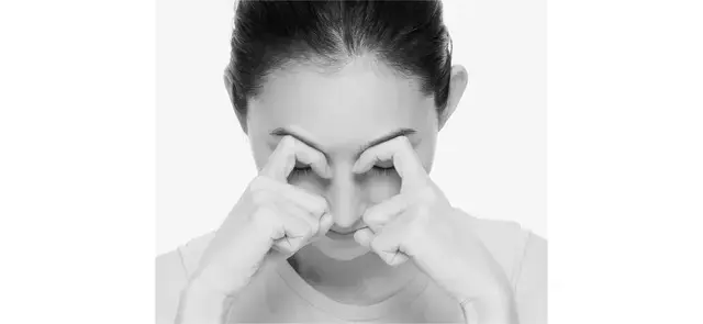 机に両肘をつき、両手の人さし指を曲げた状態で、第1関節と第2関節の間にある平らな部分を眉頭に当て、頭の重さを指にのせる。