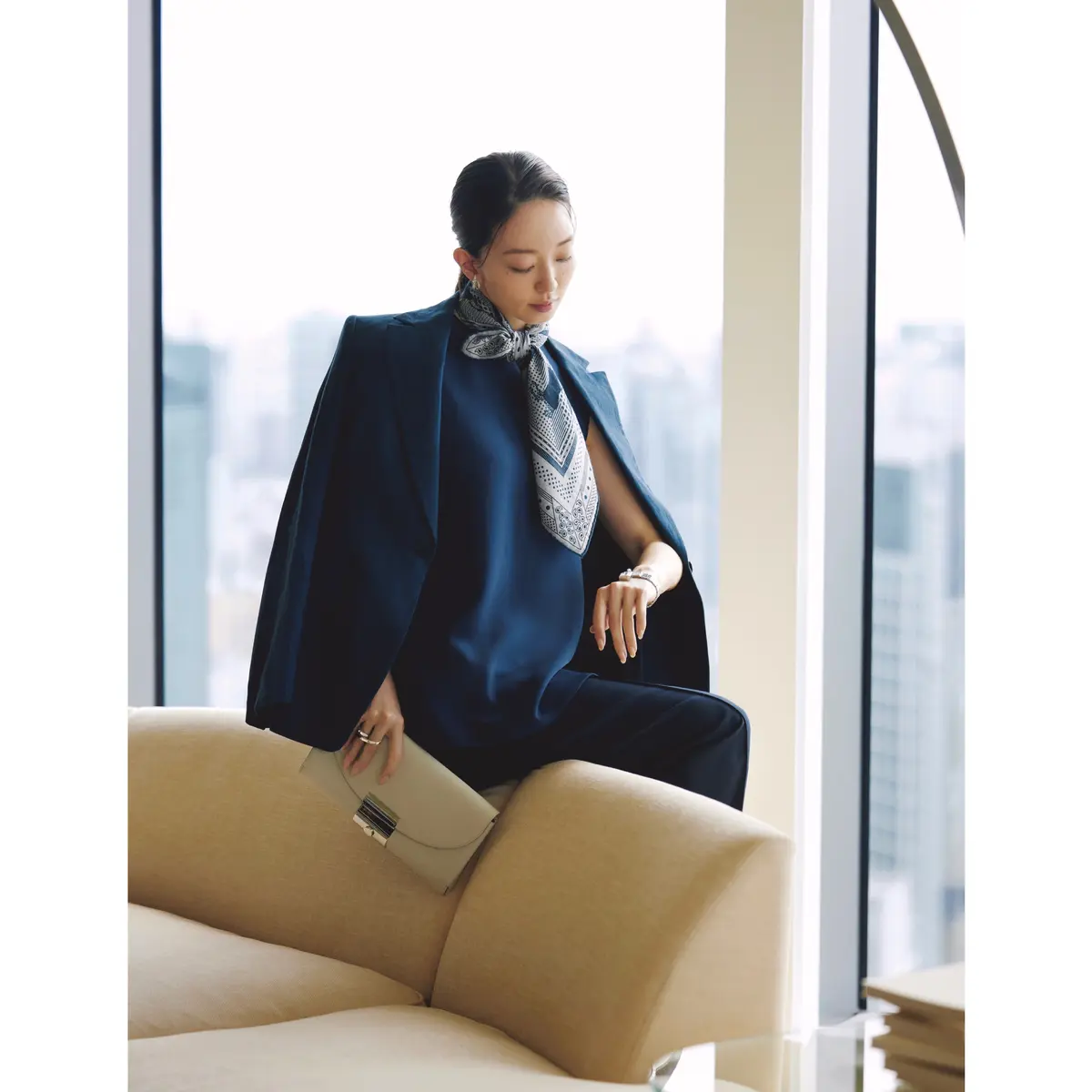 ネイビージャケットとパンツのセットアップの中にネイビーノースリーブトップスを着て、首元にブルーパネルプリントのスカーフを巻いたコーディネート　モデル・松島花