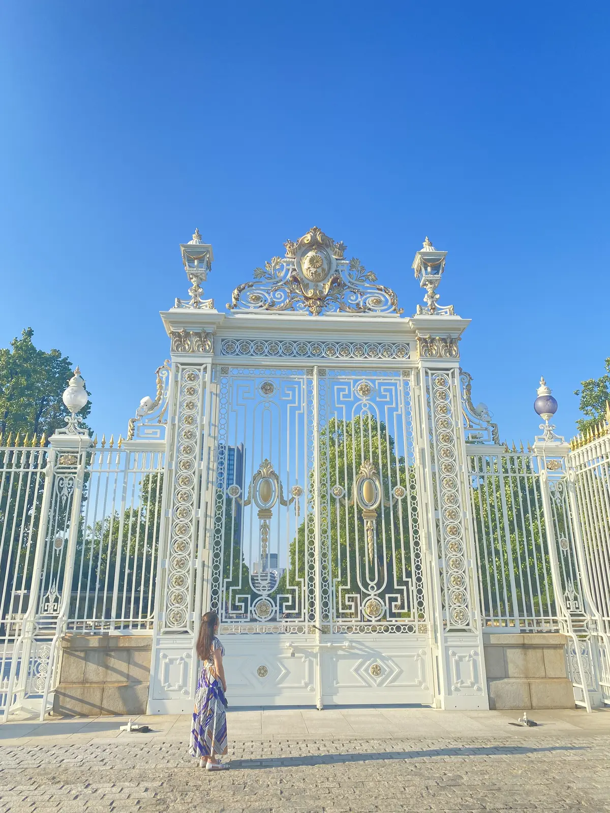 迎賓館赤坂離宮の正門前で佇む女性。白い門と青空のコントラストが印象的。