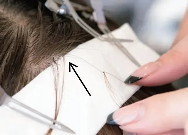 通したヘアループの結び目を締めて玉止めにし、根元へとスライドさせていく。引っぱられる感覚はあるが痛みはない。