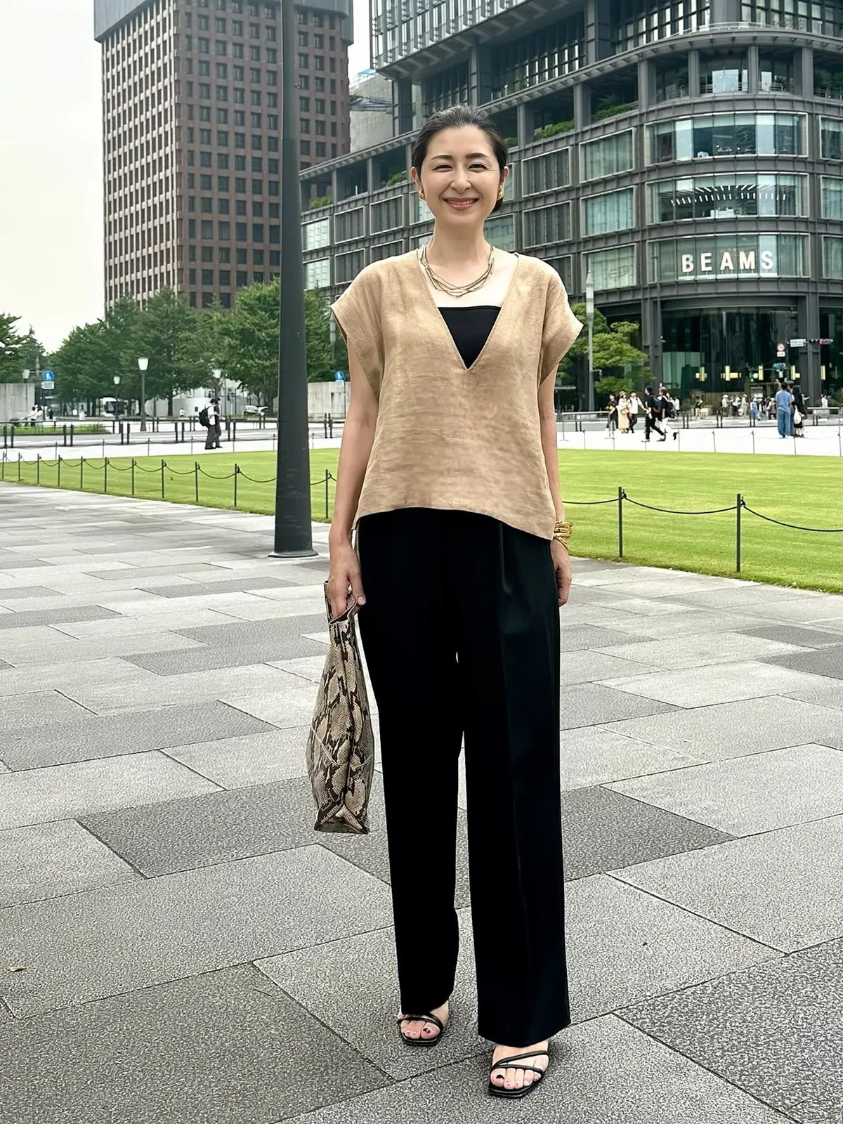 エクラプレミアムのキャメルの「リネンコンパクトジレ」、黒のタックパンツ、パイソン柄バッグ、黒のサンダル