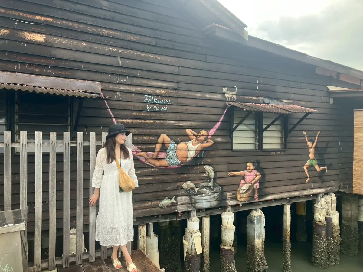 マレーシアペナン島Chew Jettyのウォールアート前で白いワンピース、旅行者に人気のユニクロのバッグを持ちポーズを撮る女性