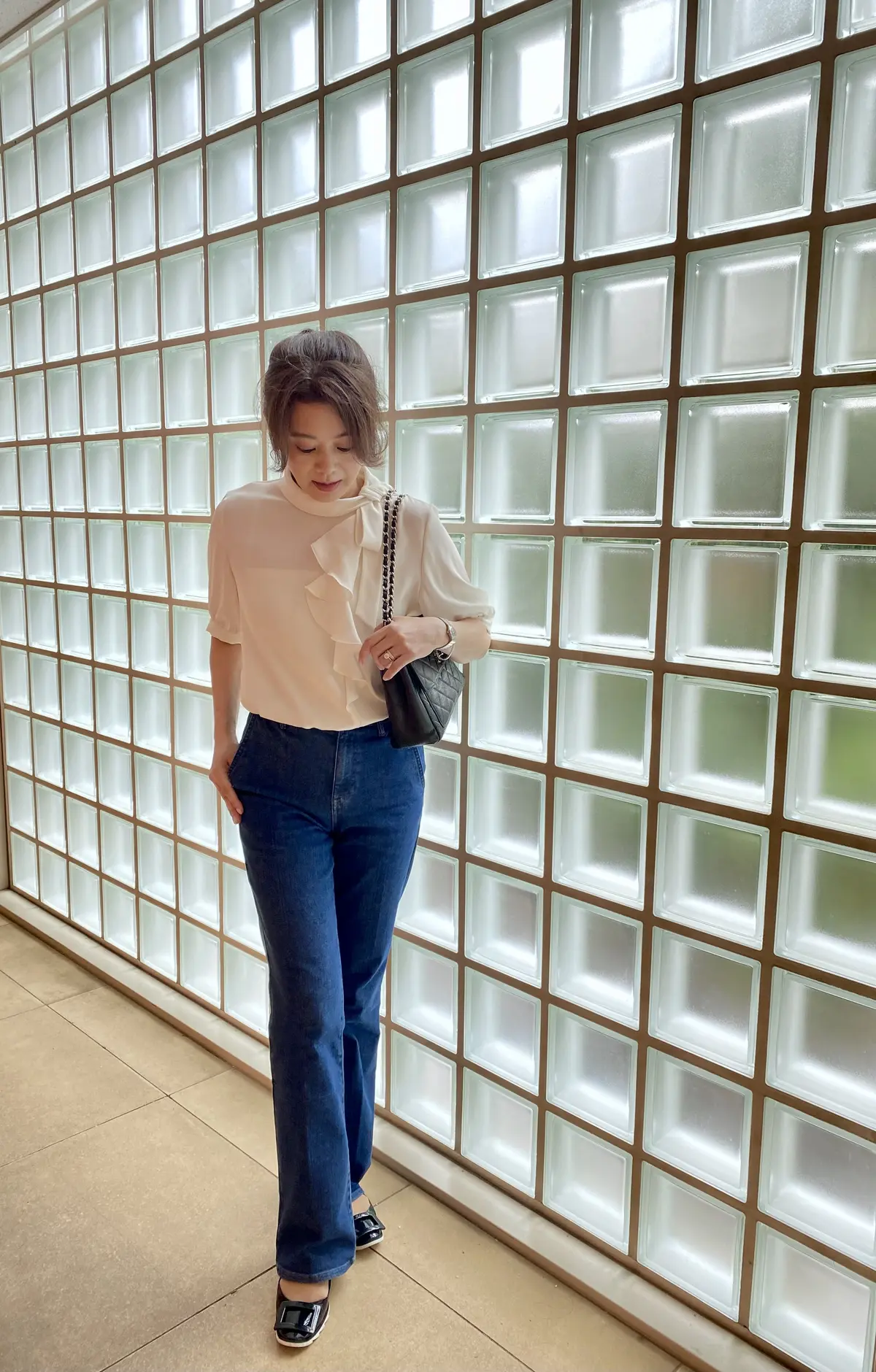 ネイビーのデニムと白のブラウスを着た女性が都会的な街角に立つ全身コーデ写真