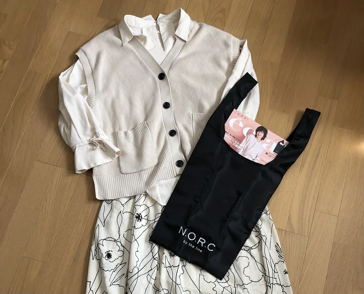 白色ブラウス　白色ニットベスト　白地に黒の模様ロングスカート　ショッパーバッグを持って立つ女性　斜め姿