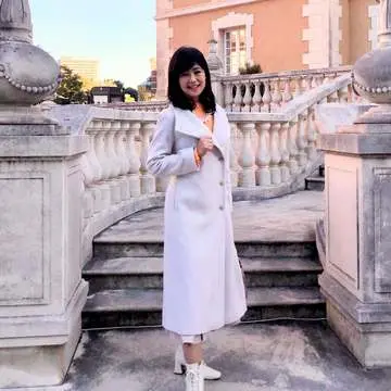 「ロペ」の白ロングコート。「リリーブラウン」のオレンジニット。「プールスタジオ アリヴィエ」の大振りパールネックレス。「ジェリービーンズ」の白ショートブーツ。