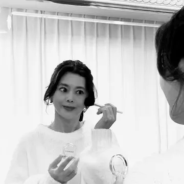 クリニーク　チークポップ 15　パンジーポップ CLINIQUE CHEEK POP  PANSY POP15をイタリア製の鏡に向かって塗る髪をまとめ白いセーターを着た女性のモノクロ写真