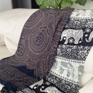 エスニックな象柄とペイズリー柄のタイパンツを、白いソファにかけてスタイリング。奥に映る大ぶりの観葉植物が南国ムードを引き立て、くつろぎの午後を思わせる1枚に。