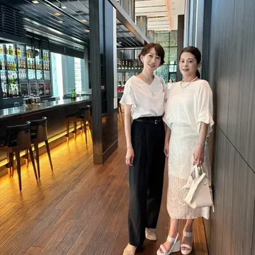 白トップスと黒パンツの女性と、白いスカートの女性がホテル内で並んでポーズ。