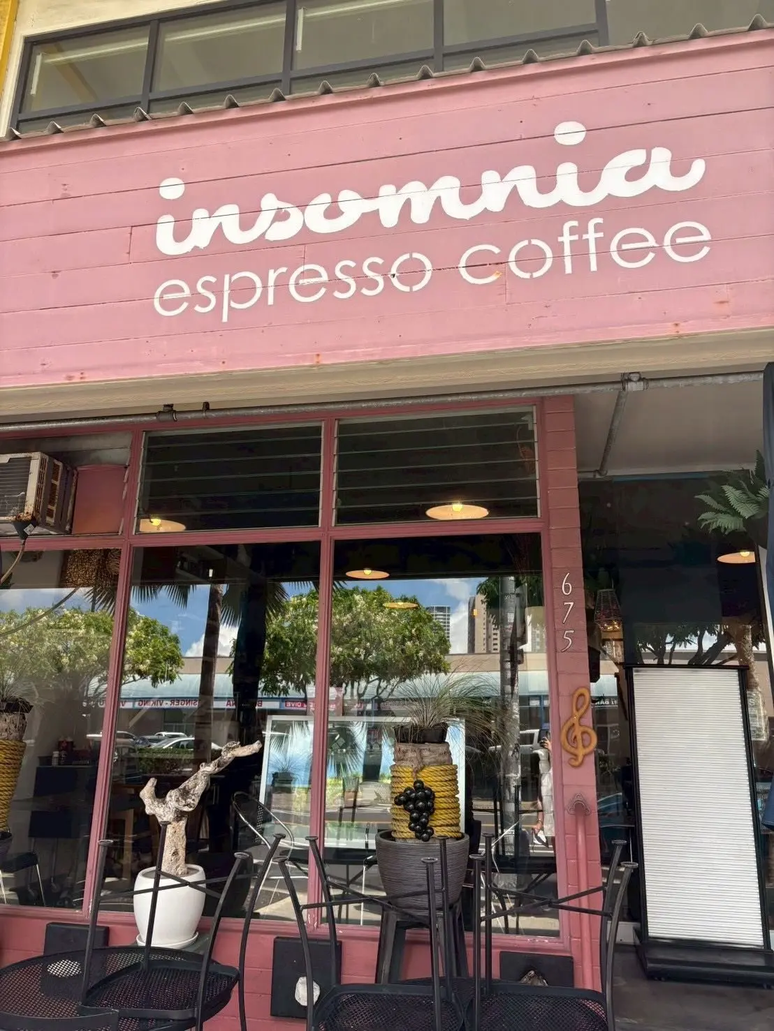 ピンクの壁に「insomnia espresso coffee」と書かれたカフェの外観。ガラス窓から中が見え、屋外のテーブルと椅子が配置されている。