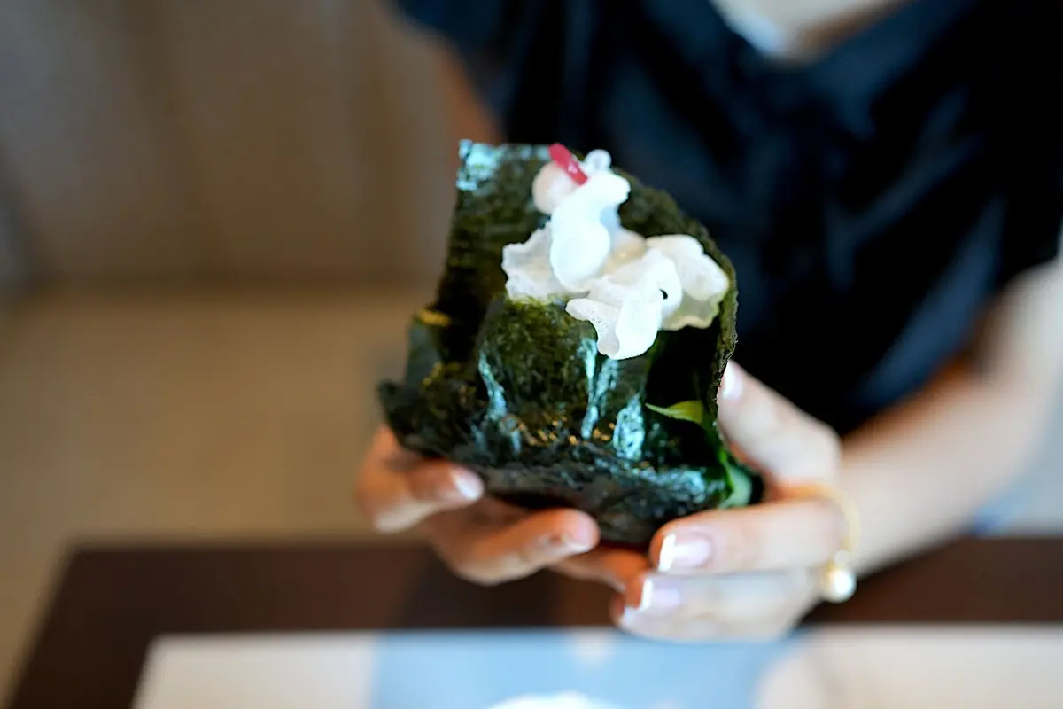 手で支えられた海苔巻き。中には白いクリーム状の食材と、赤い飾り付けが施されている。