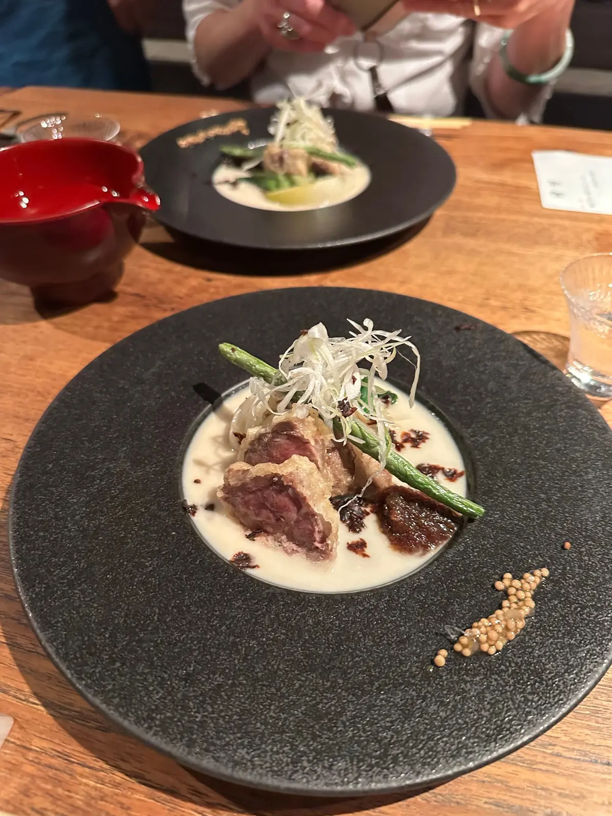 黒いプレートに、クリームソースの上にアスパラガスと肉がのった料理。小豆とスライスした野菜が添えられています。