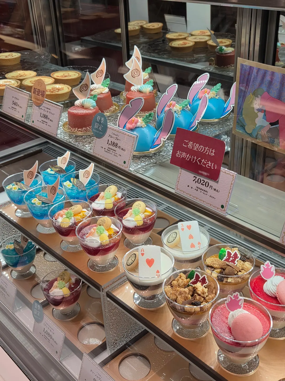 ショーケースに並んだ、春らしいデコレーションのスイーツ。ピンクやパステルカラーのケーキ、カップに入ったゼリー、マカロンなどが並び、中央にはウサギの置物がある。価格表示も見える。