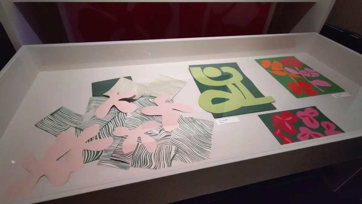 白い展示ケースに収められた、複数の版画作品。左にはピンク色の花と縞模様の作品、右には緑と黄緑、赤と緑、赤と黒の抽象的なデザインの作品が並んでいる。