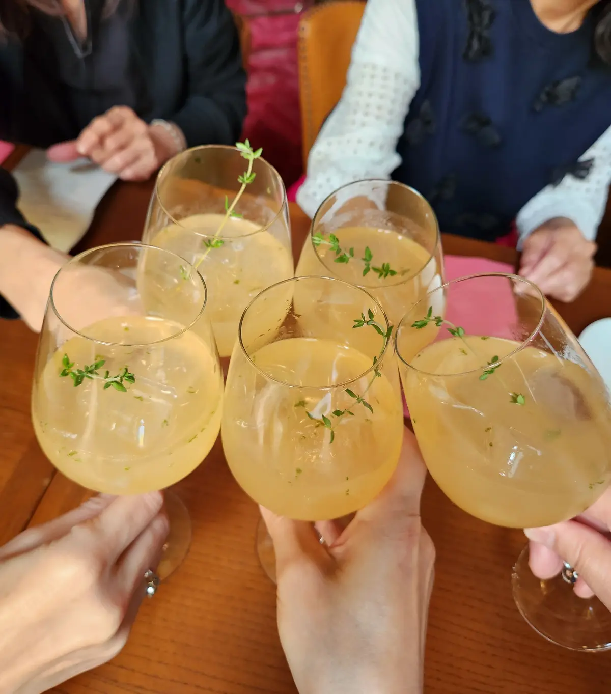 ガラスカップ5つに、黄色い飲み物と緑のハーブの装飾が並んでいる