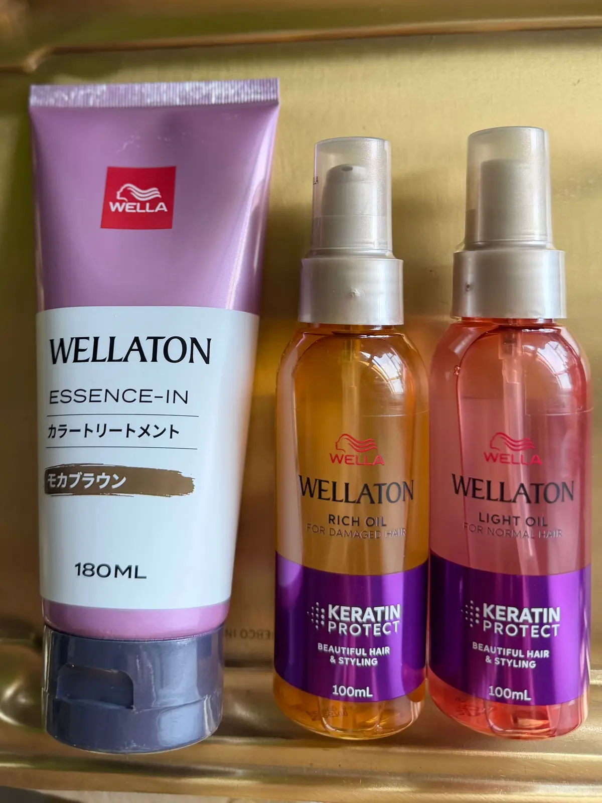ウェラ（WELLA）のヘアケア製品3点。左は紫色のチューブ容器に入った「エッセンスイン」、中央と右はオレンジ色のボトルに入ったオイル。それぞれ「リッチオイル（ダメージヘア用）」、「ライトオイル（ノーマルヘア用）」の表記がある。