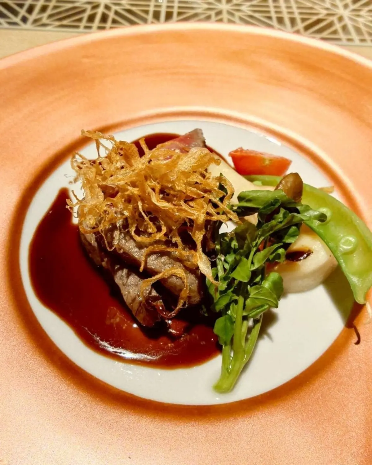 白いプレートに、赤ワインソースをかけたステーキ
