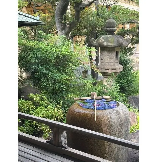 石造りの灯篭と青い花が咲く石の容器、木製の杭が背景の庭園に設置されている
