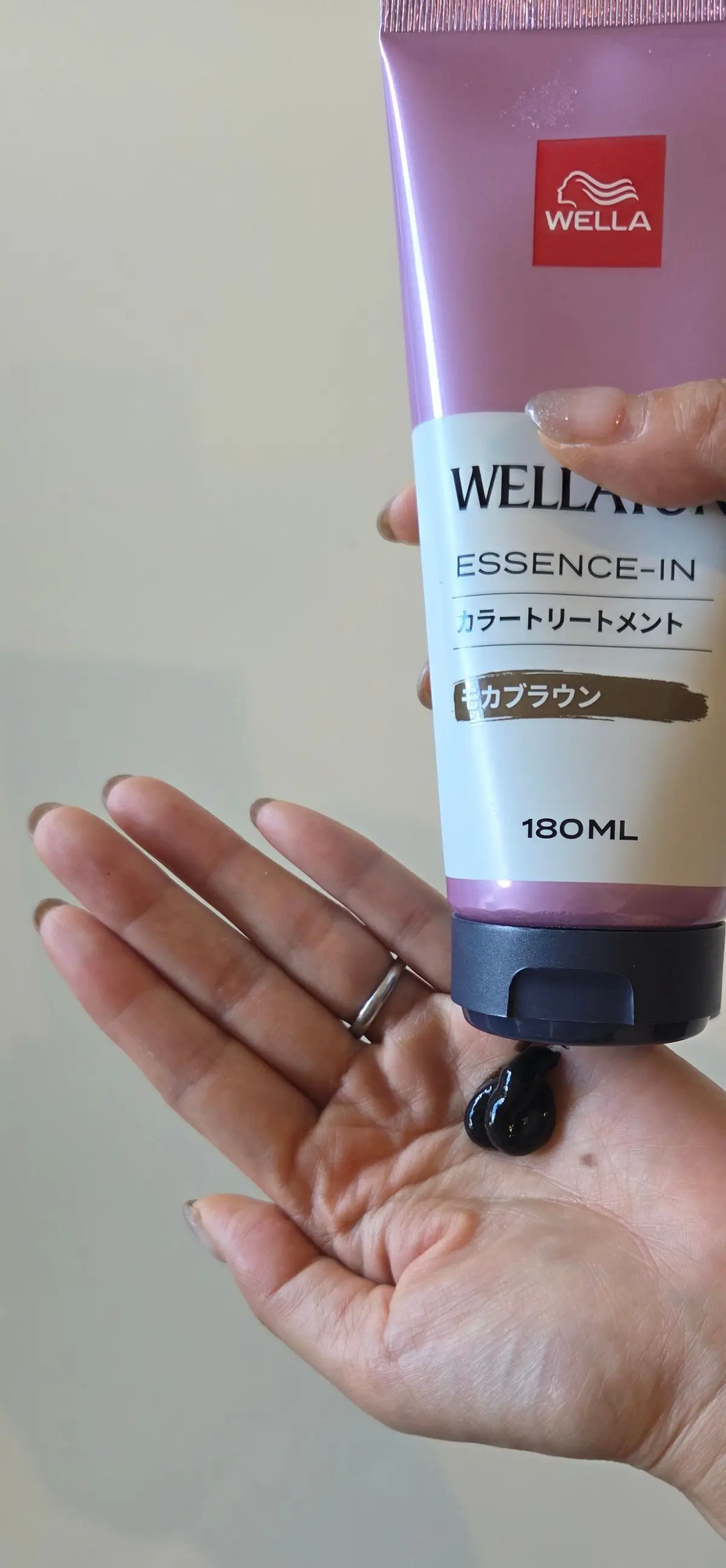 手のひらに乗った、ウェラ（WELLA）のエッセンスインカラートリートメントの180mlチューブ。ピンクと紫色のグラデーションのパッケージで、茶色の文字で製品名と「カブラウン」の表記がある。