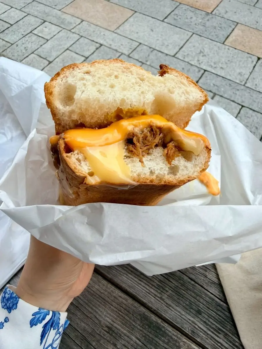 スモークチキンとチーズがたっぷり入ったサンドイッチが、紙の包み紙に包まれて木製テーブルに置かれている。
