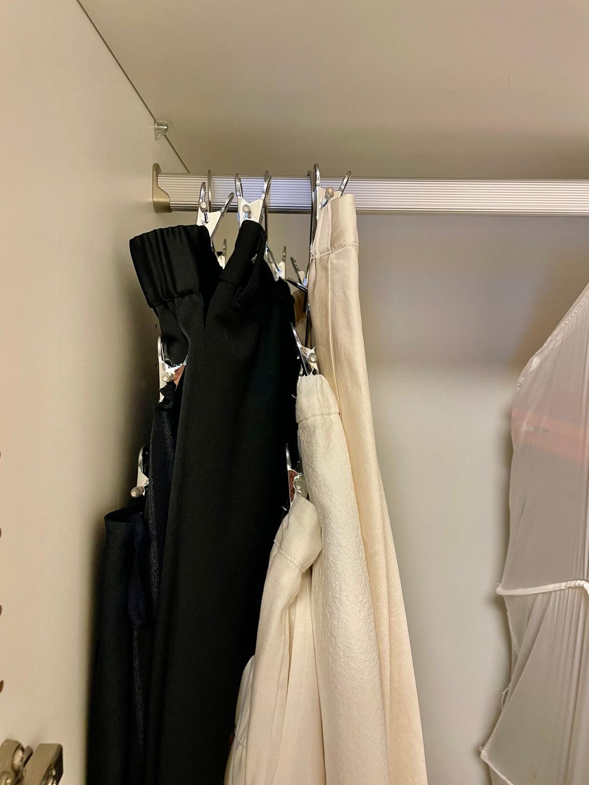 クローゼットのポールに、黒い服や白いシャツが複数のハンガーに掛かっている様子。壁はベージュ色で、シンプルな収納空間。