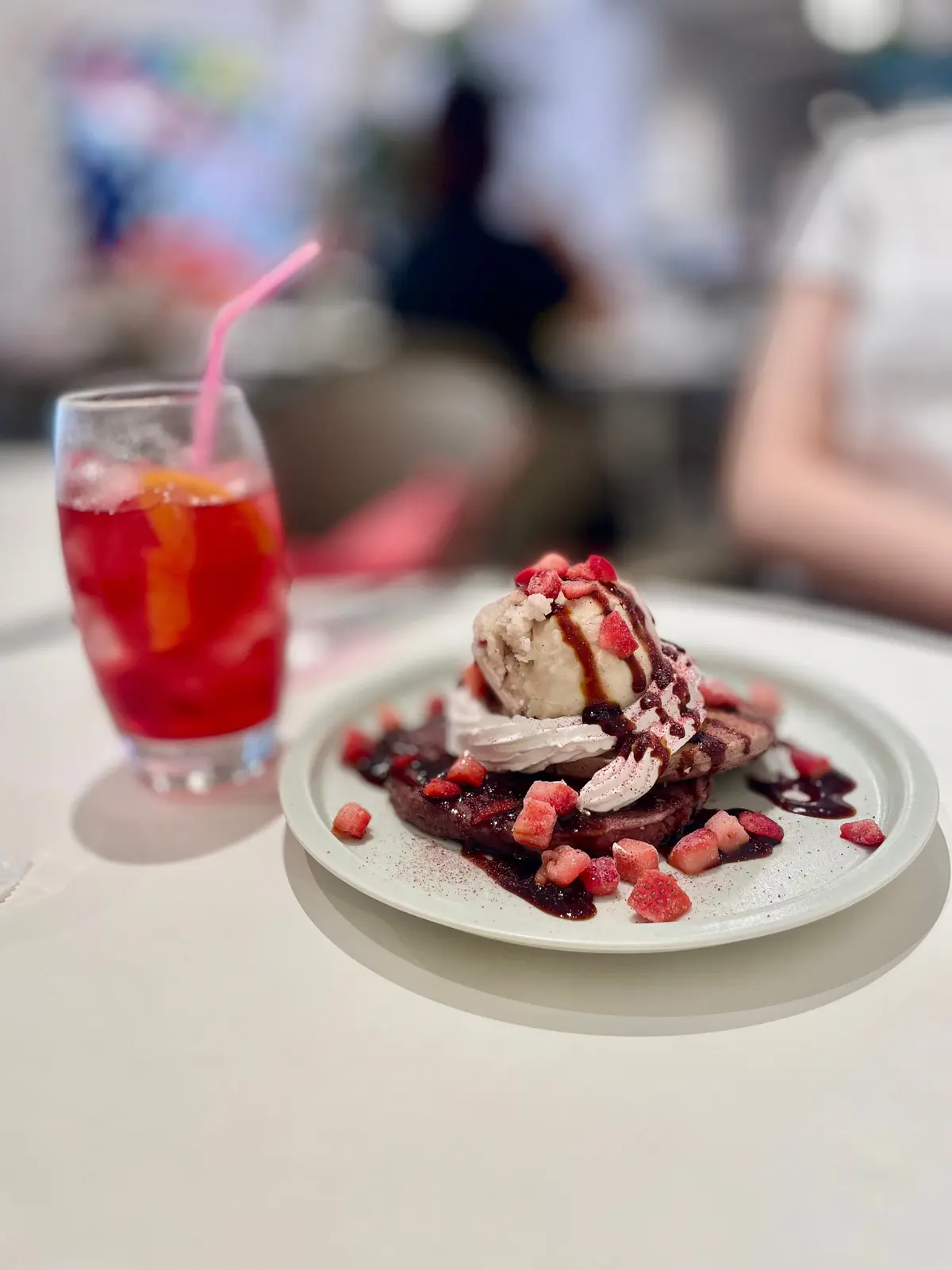 ベリーソースとクリームをトッピングしたパンケーキと、赤いフルーツジュースが注がれたグラスが並ぶ