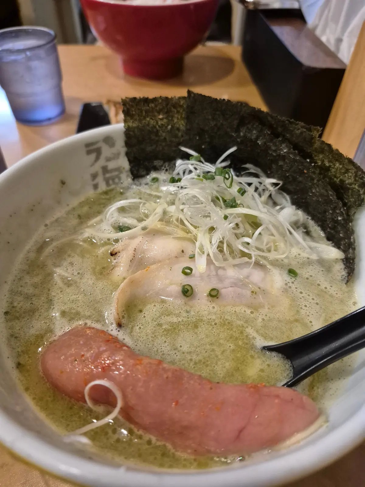 ラーメンの湯気立つ一杯。白濁したスープに、チャーシュー、海苔、ネギ、メンマが浮かび、黒い箸が添えられている。