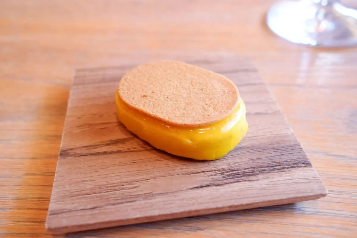 木製の板の上に置かれた、パンケーキと黄色のクリームの詰め合わせ。パンケーキは丸みを帯びた楕円形で、クリームは鮮やかな黄色をしている。