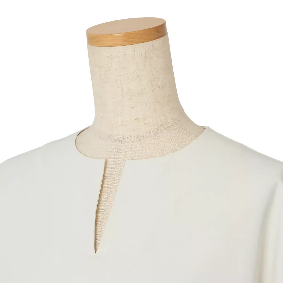 白い布製のマネキンに、オフホワイトのシンプルなVネックの服が着用されている。首元に細長いV字の切り抜きがある。