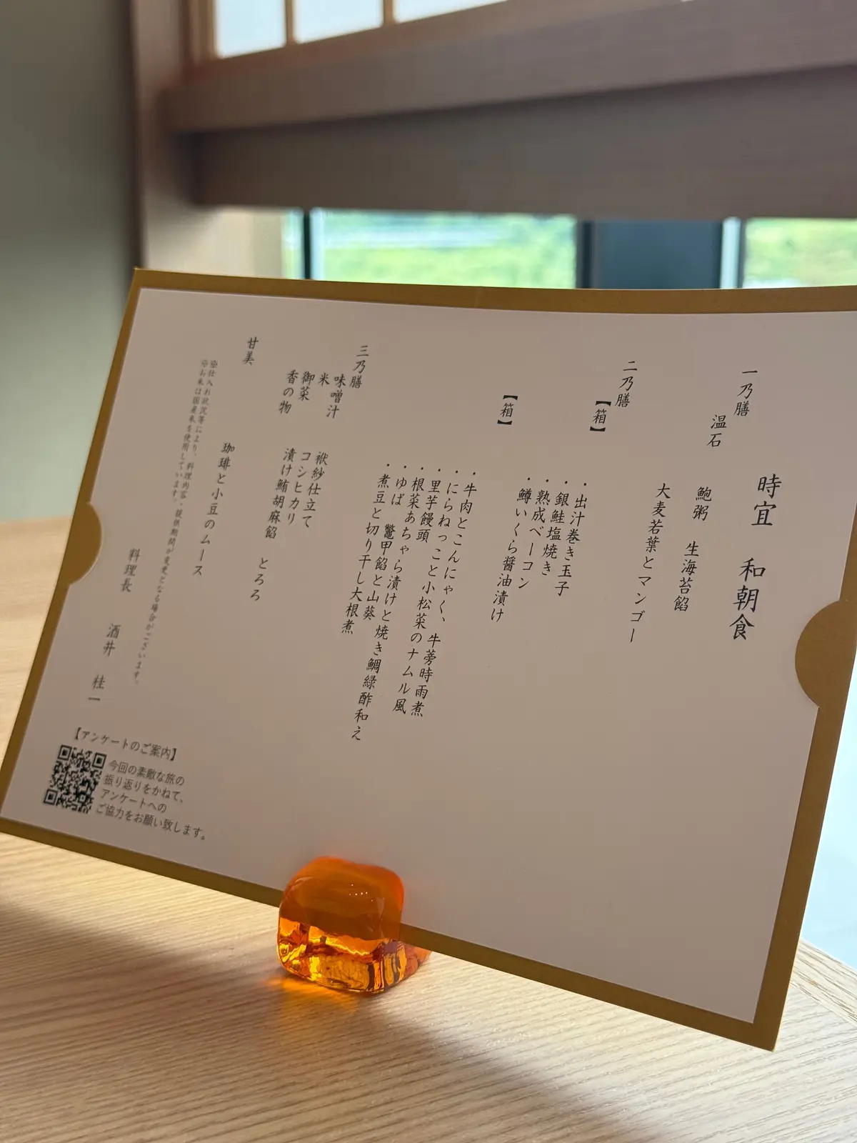 金縁のカードに日本語で記載されたメニューと、木製テーブル上に置かれたオレンジ色のアメ玉