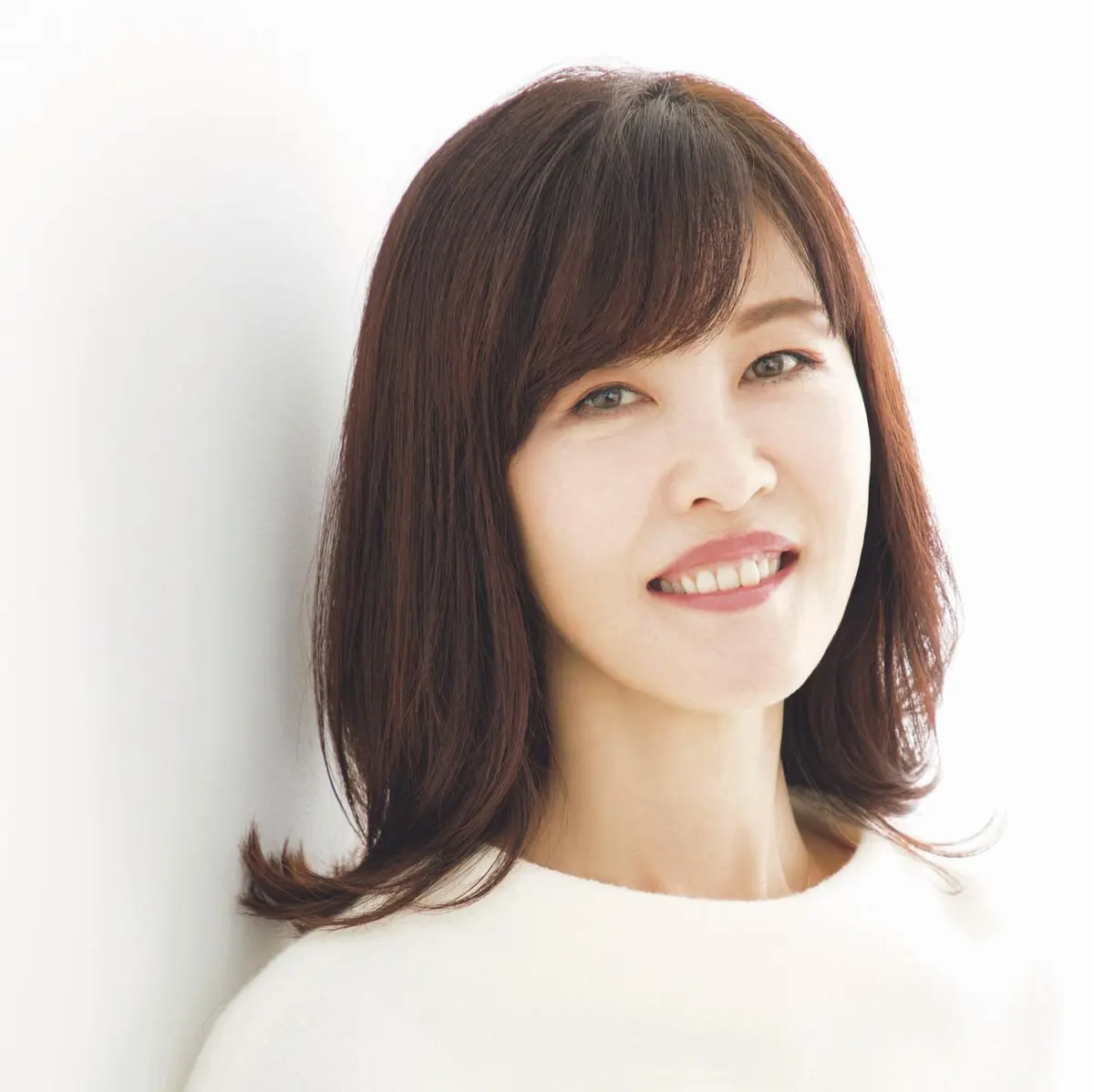 美容ジャーナリスト 安倍佐和子さん　の女性が白い壁に寄りかかり、明るい表情で微笑んでいる