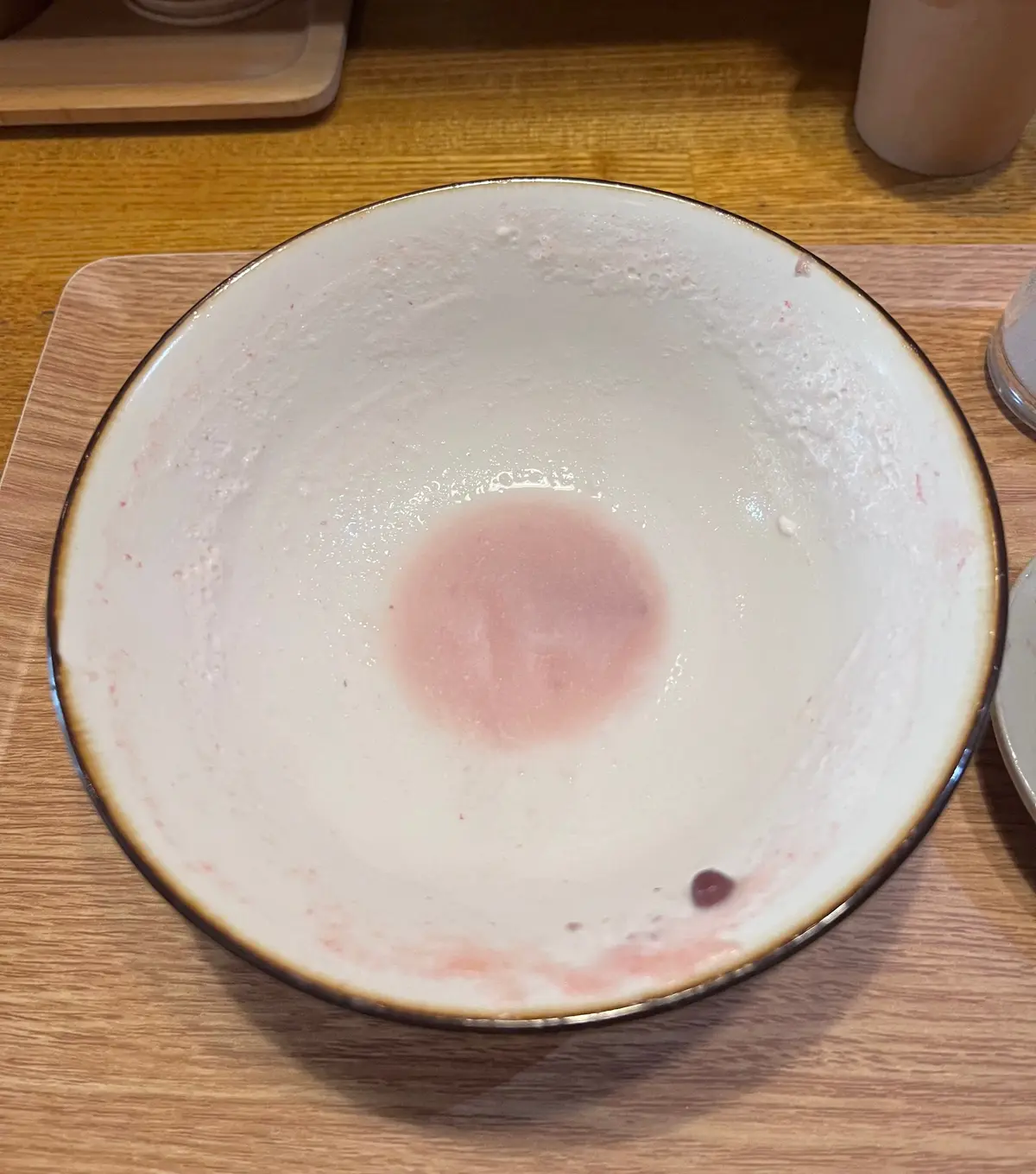 木製のテーブルに置かれた、内側にピンク色、外側に茶色の縁取りのある白い陶器の皿。皿の中央にはピンク色の染みが残っている。