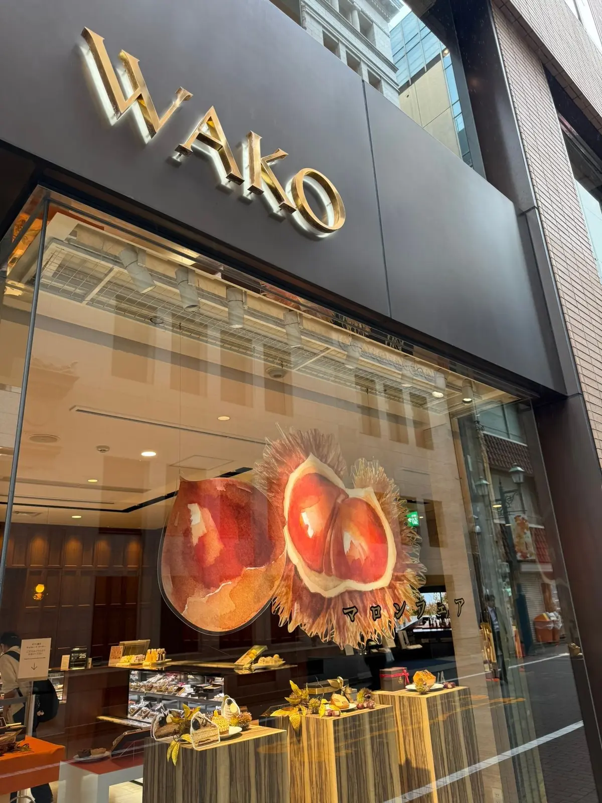 百貨店和光のショーウィンドウ。栗を模した大きな装飾品が中央に飾られ、その下には栗菓子が並んでいる。背景に都市の建物が見える。