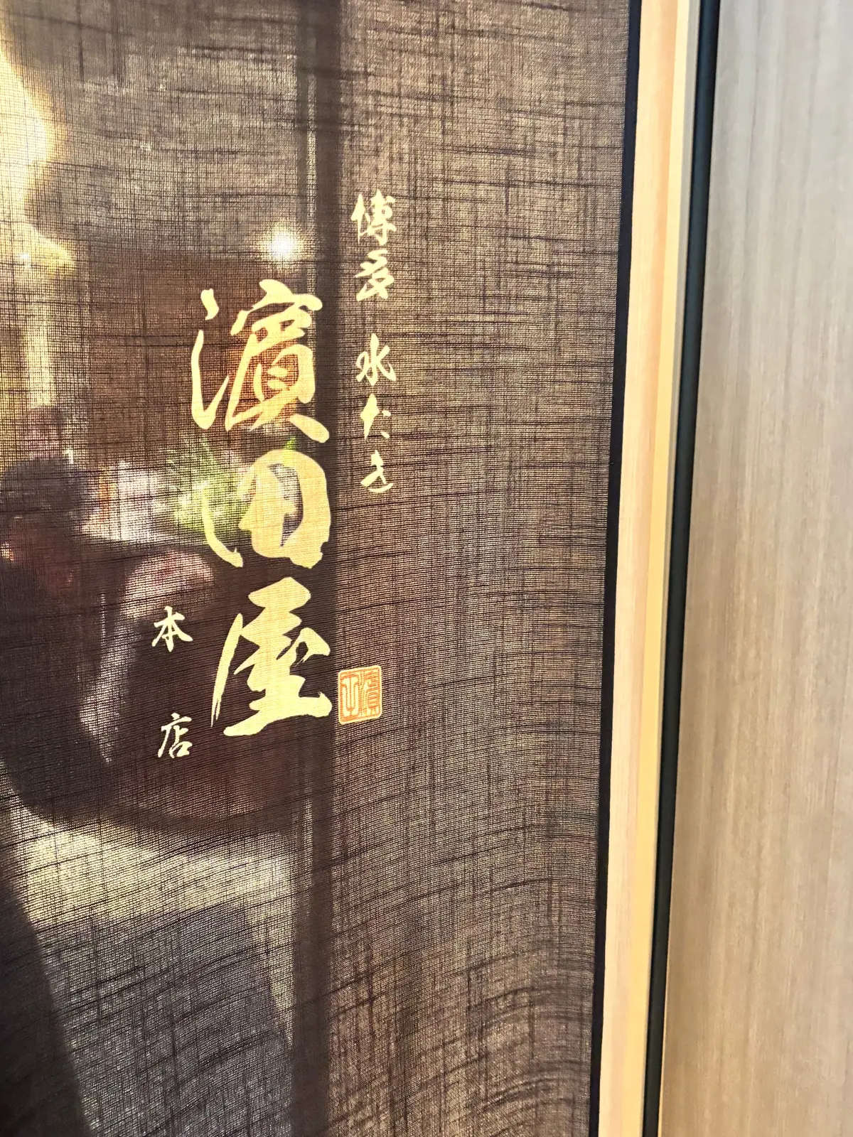 茶色の布地に、赤い文字で「溪和屋」と書かれた看板。右上に小さく「傳」という文字、下部に「本店」とある。左側には人物のシルエットが描かれている。