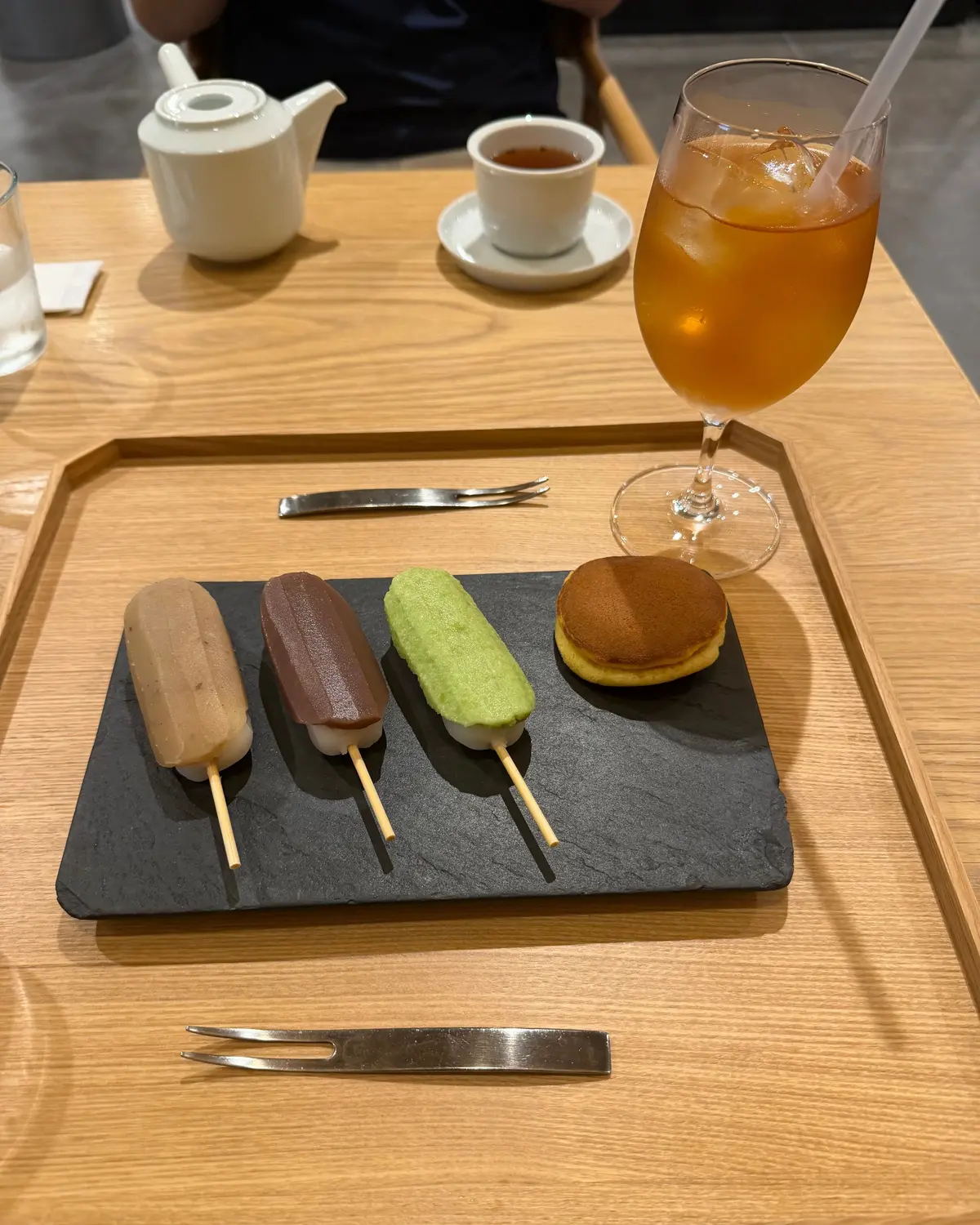 木製のトレイに置かれた、お茶、コーヒー、かき氷、丸いお菓子。かき氷は3色（ベージュ、紫、緑）で、それぞれ竹串が刺さっている。コーヒーは白磁のカップに、お茶は白磁のポットに入っている。