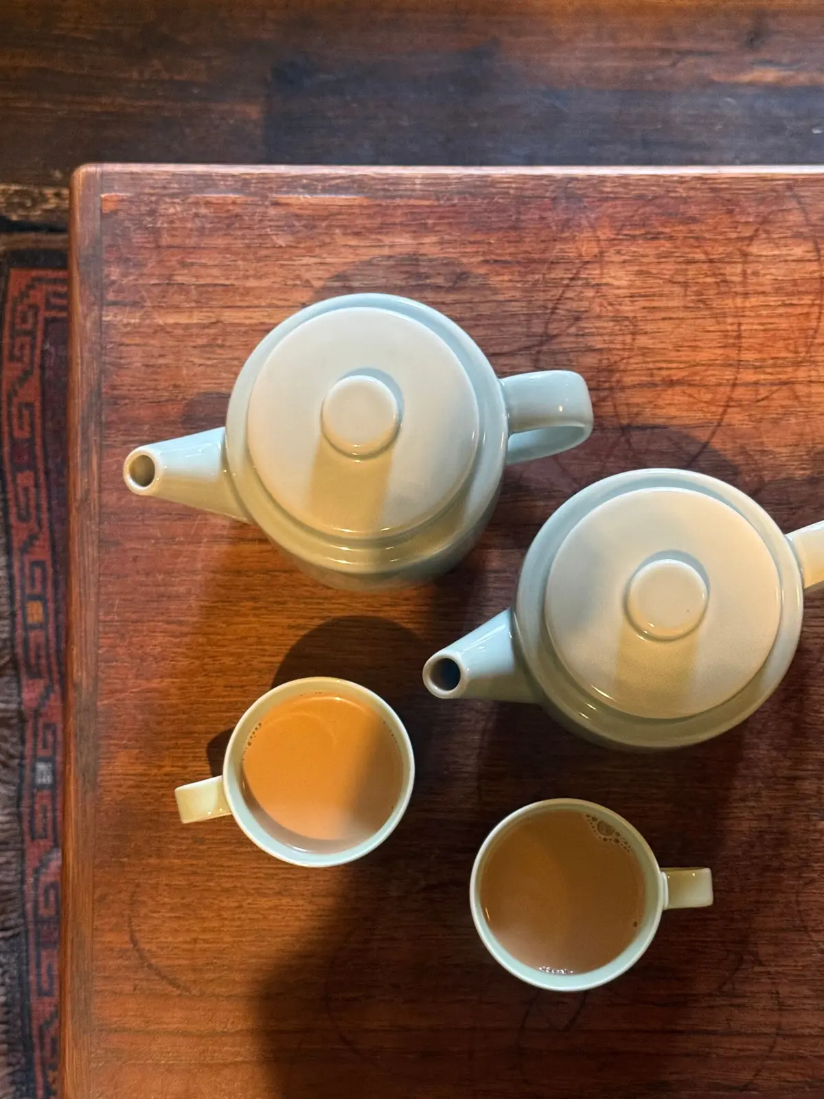 木製のトレイに置かれた、淡いグレーの急須と湯呑み2つ。湯呑みには茶色の飲み物が注がれている。急須は丸みを帯びた形。トレイには模様が施されている。
