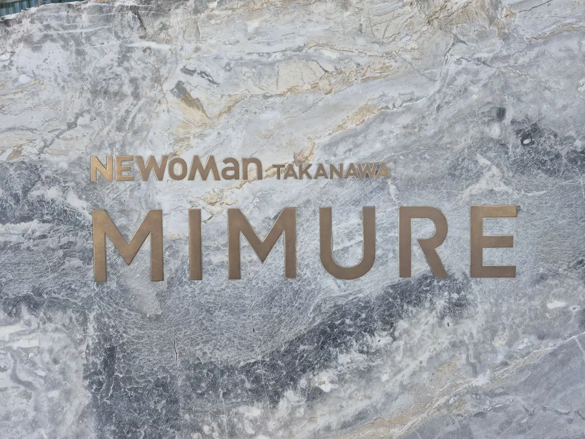 グレーの石材に、金色で「MIMURE」の文字が浮き出ている。上部には「NEWoMan TAKANAWA」のロゴが小さく配置されている。