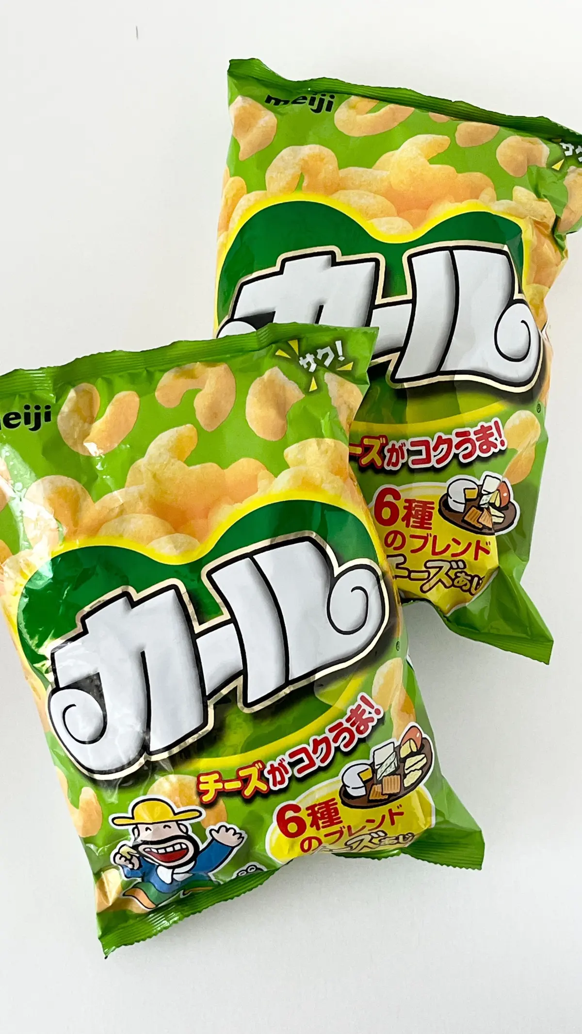 緑色のパッケージに白文字で「カービー」のロゴが描かれた、お菓子「カービー」の袋が3つ並んでいる写真。中身は黄色い丸いスナック菓子。パッケージには「6種類のプリントチーズがコクラ！」の文字と、キャラクターのイラストがある。