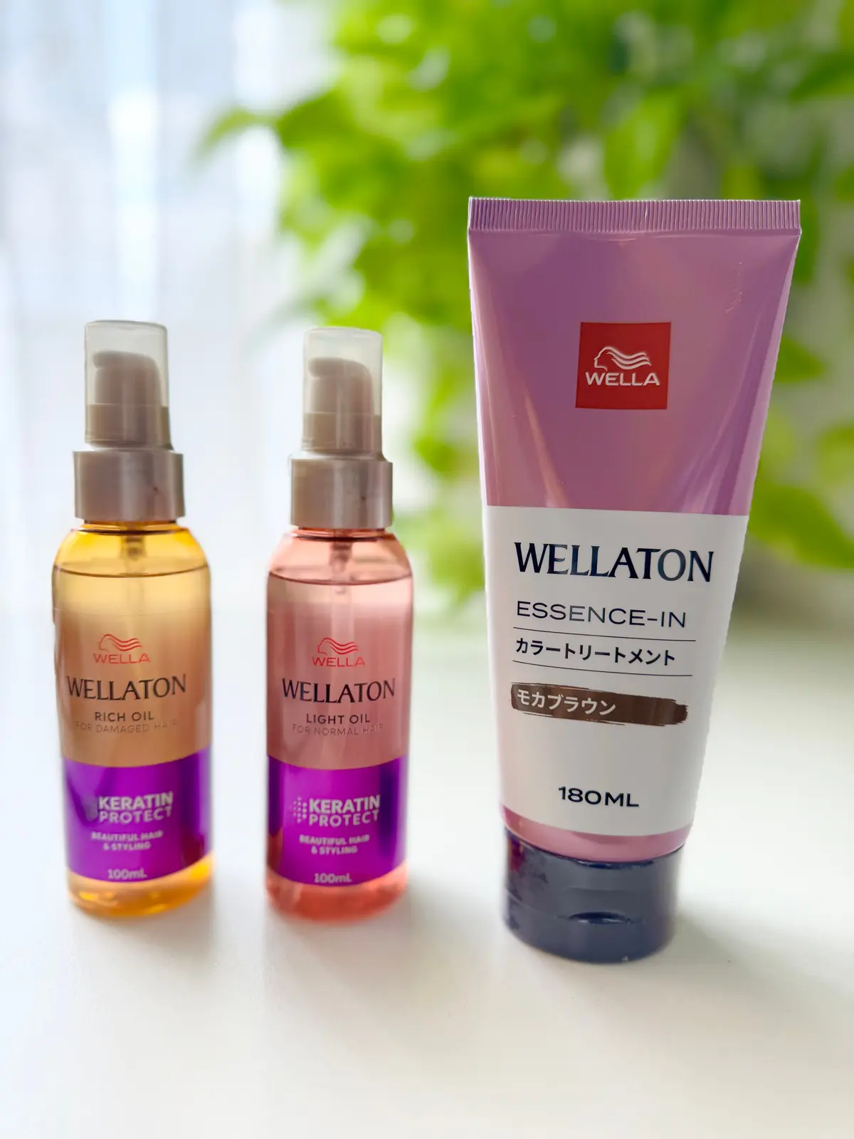 ウェラ（WELLA）のヘアオイルとトリートメントメント。左から、濃いオレンジ色のリッチオイル、薄いオレンジ色のライトオイル、ピンク色のエッセンスイン。いずれも100mlまたは180mlの容量。背景は緑色のボケ。