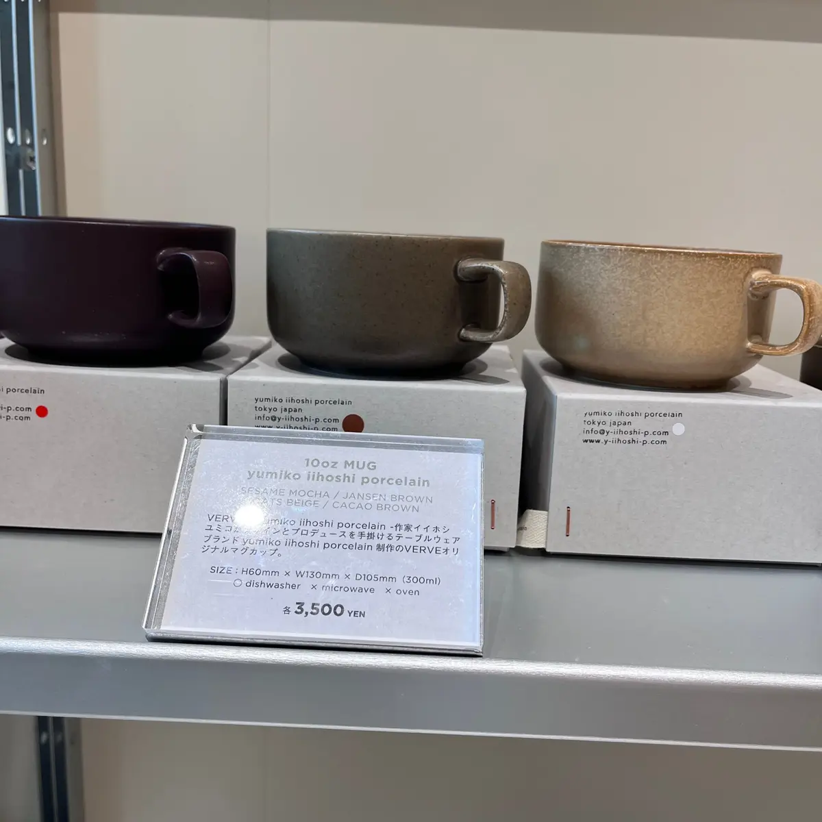 yumiko iihoshi porcelainの陶器マグカップ3つが並んでいる写真。
それぞれ異なる色（白、ベージュ、茶色）で、縦長の円柱形。
マグカップの裏にはブランド名とウェブサイトの記載がある。
価格は1つ3,500円。