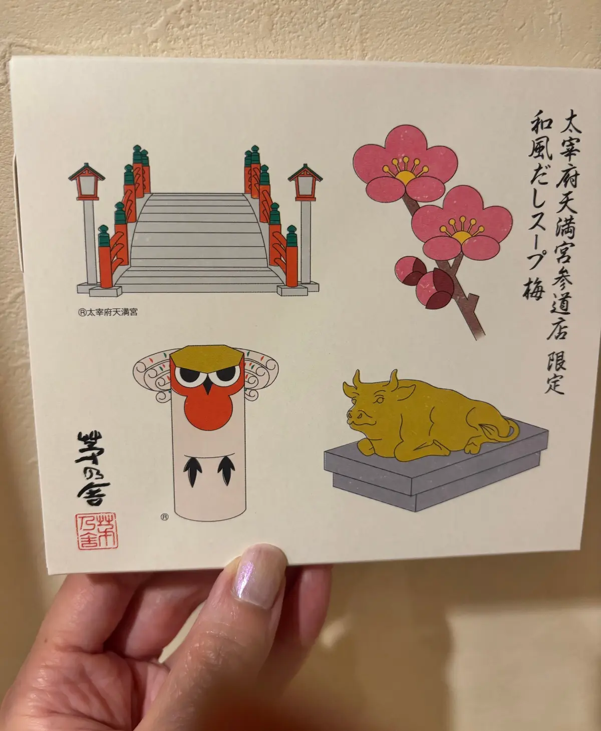 淡いクリーム色の箱に、日本の伝統的なモチーフが描かれている。鳥居、桜の花、柱に止まるフクロウ、台座に寝そべる雄牛のイラスト。箱の右側には日本語の文字が縦書きで配置されている。箱の左下には「豊鳥舎」のロゴマーク。