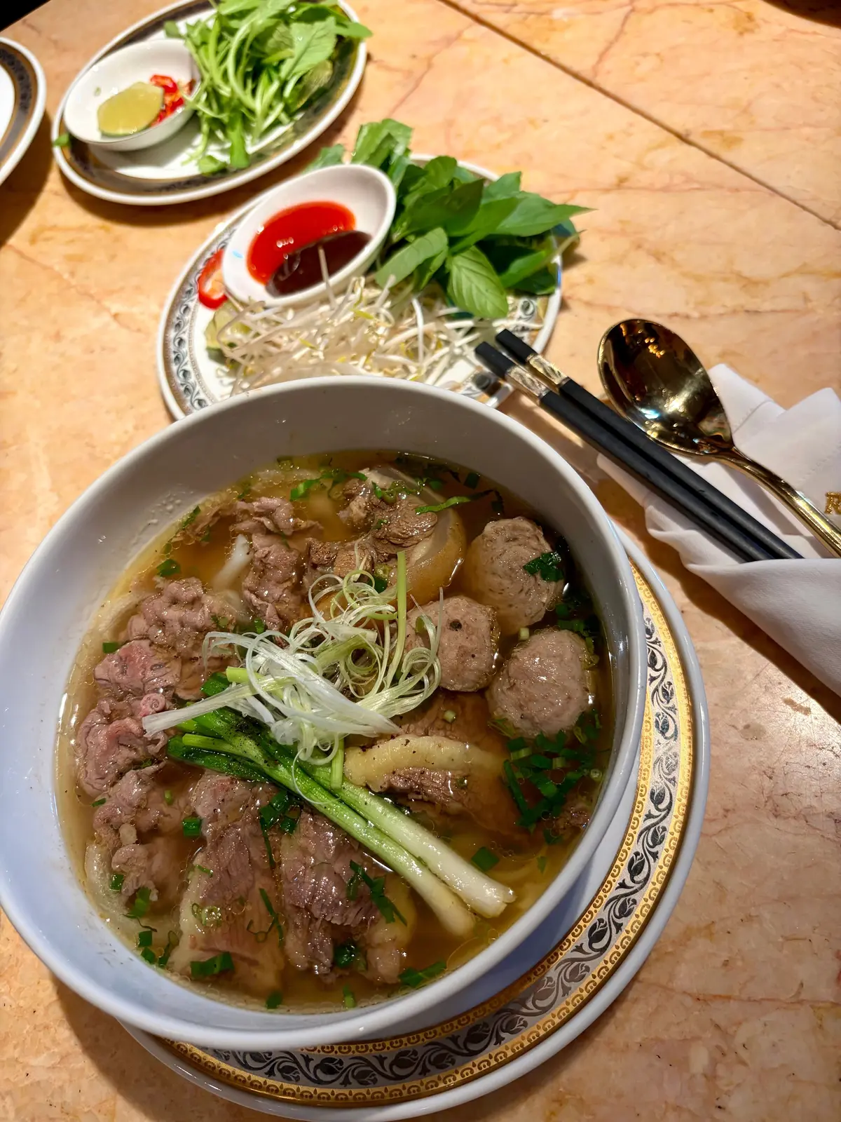 白いボウルに、牛肉と豆腐、ネギ、豆もやしをトッピングしたスープが盛り付けられたフォー、周囲にはハーブや調味料の小皿が置かれている