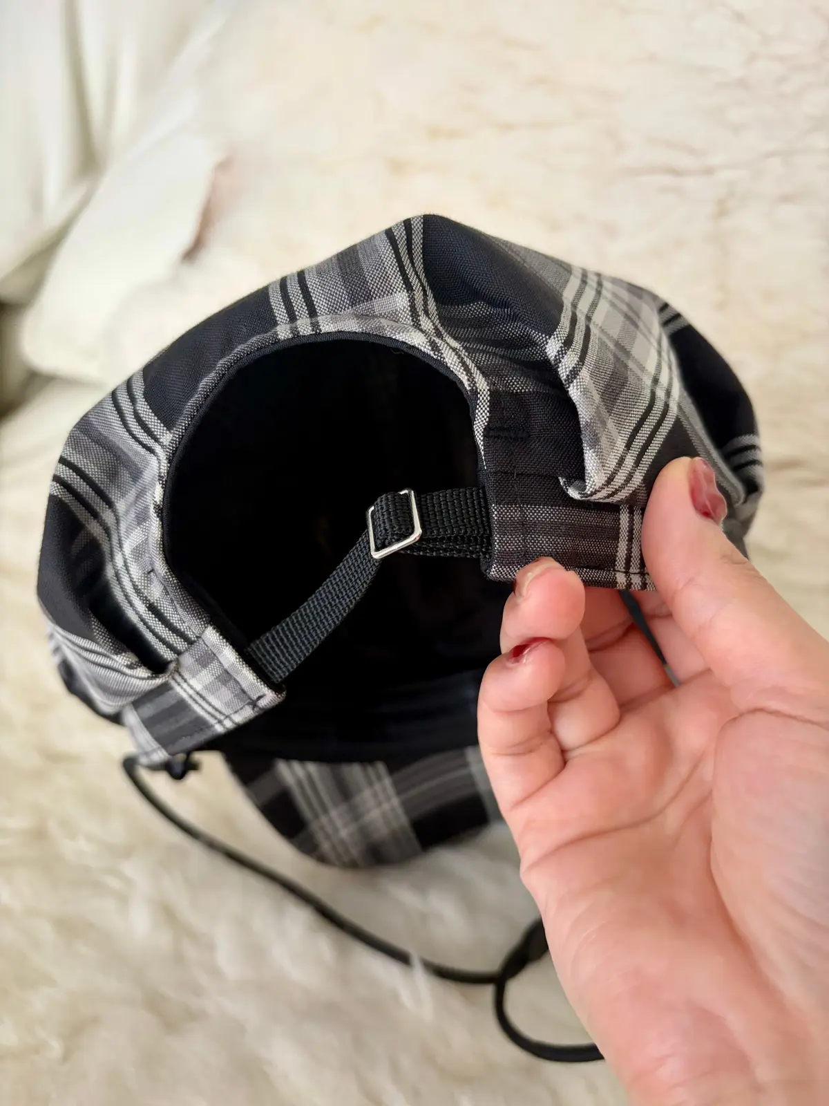 黒と白のチェック柄キャップの内側。黒い調節可能なストラップとバックルが見える。手でストラップを握っている。