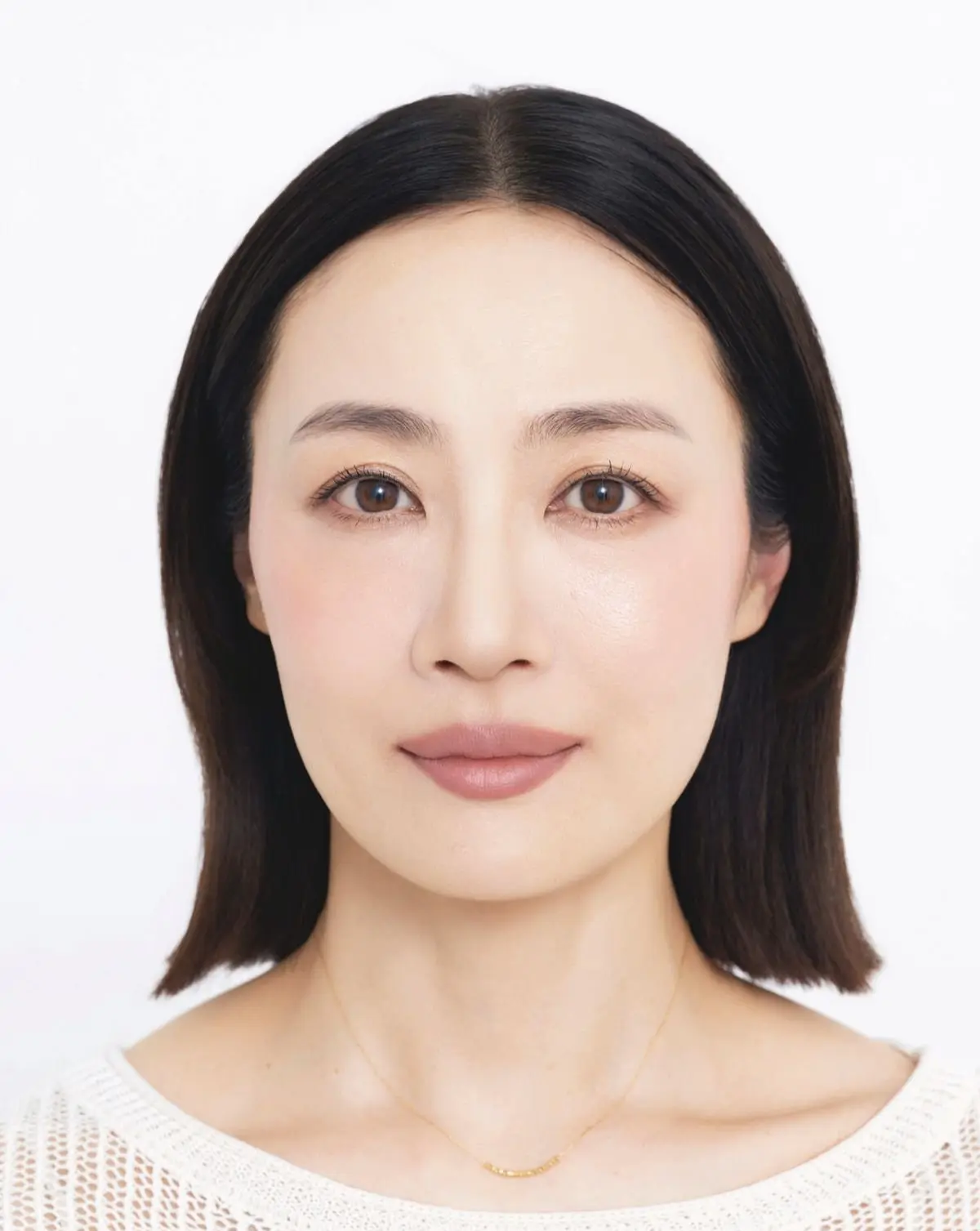 Before 黒髪ショートカットの女性が白い背景に映り、シンプルな白い編み込みセーターを着て細い金のネックレスを身につけている