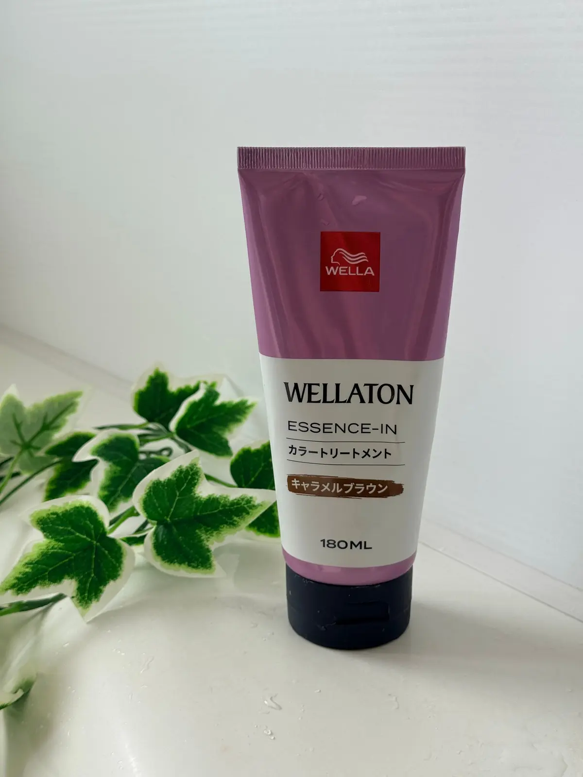 ウェラ(WELLA)の「ウェラトーン エッセンス・イン カラーリートメント」180mlのピンク色のチューブ。手前に緑の葉が置かれている。