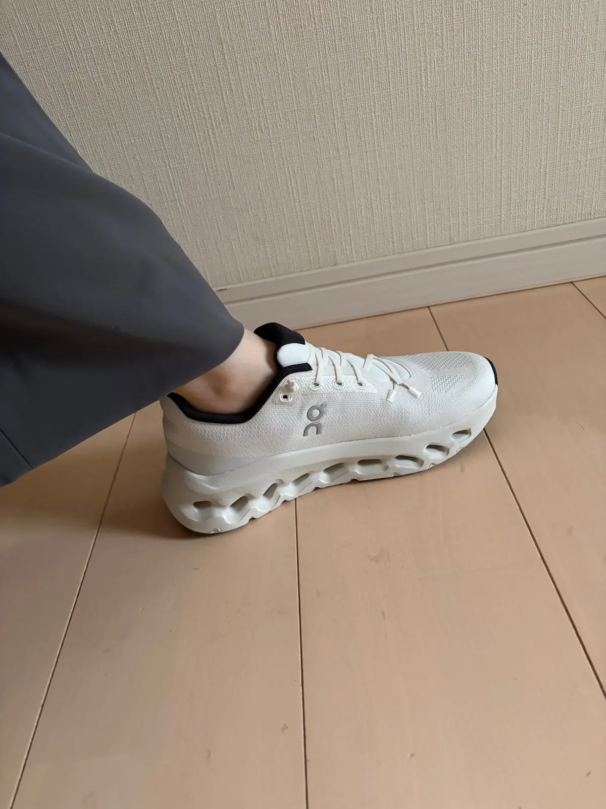 灰色のズボンを履いた足元に、白いOnのウォーキングシューズ。靴底は特徴的な形状で、白いシューレースがほどこされている。