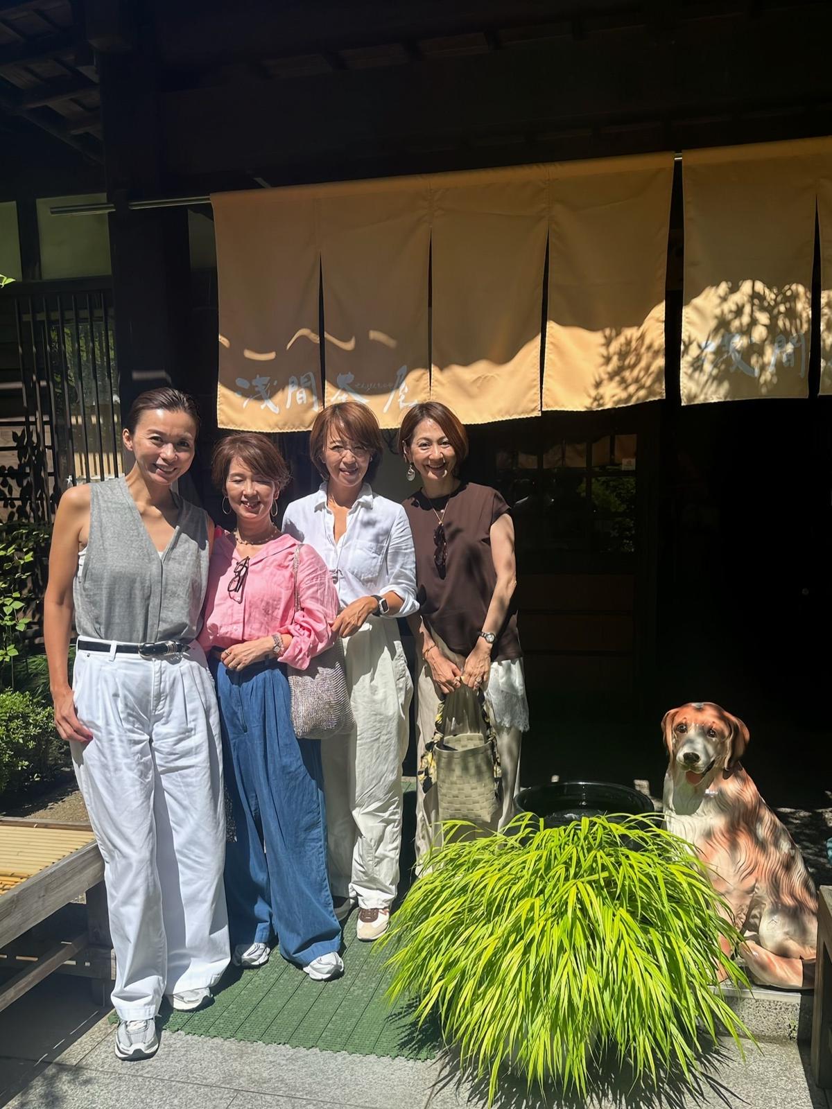 屋外で、5人の女性が笑顔で写っている。左から、グレーのタンクトップに白いパンツ、ピンクのシャツに青いパンツ、白いシャツにベージュのパンツ、黒いシャツにベージュのスカート、そして白いシャツにベージュのパンツを着用。