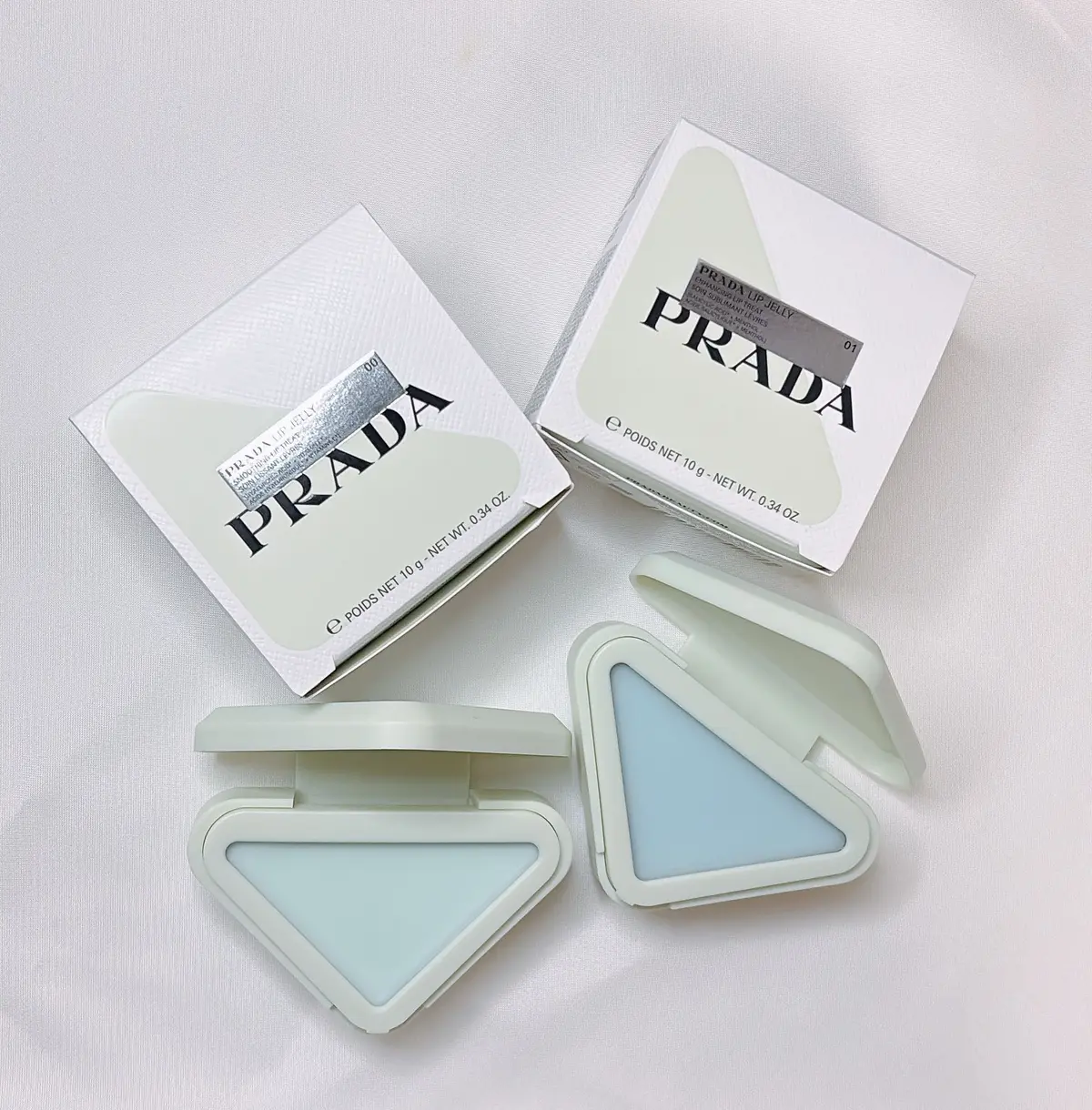 PRADAのリップジェリー、色番号01。半透明の淡いブルーグリーンがかった色合いで、三角形のコンパクトに入っている。箱とコンパクトが並んで置かれている。