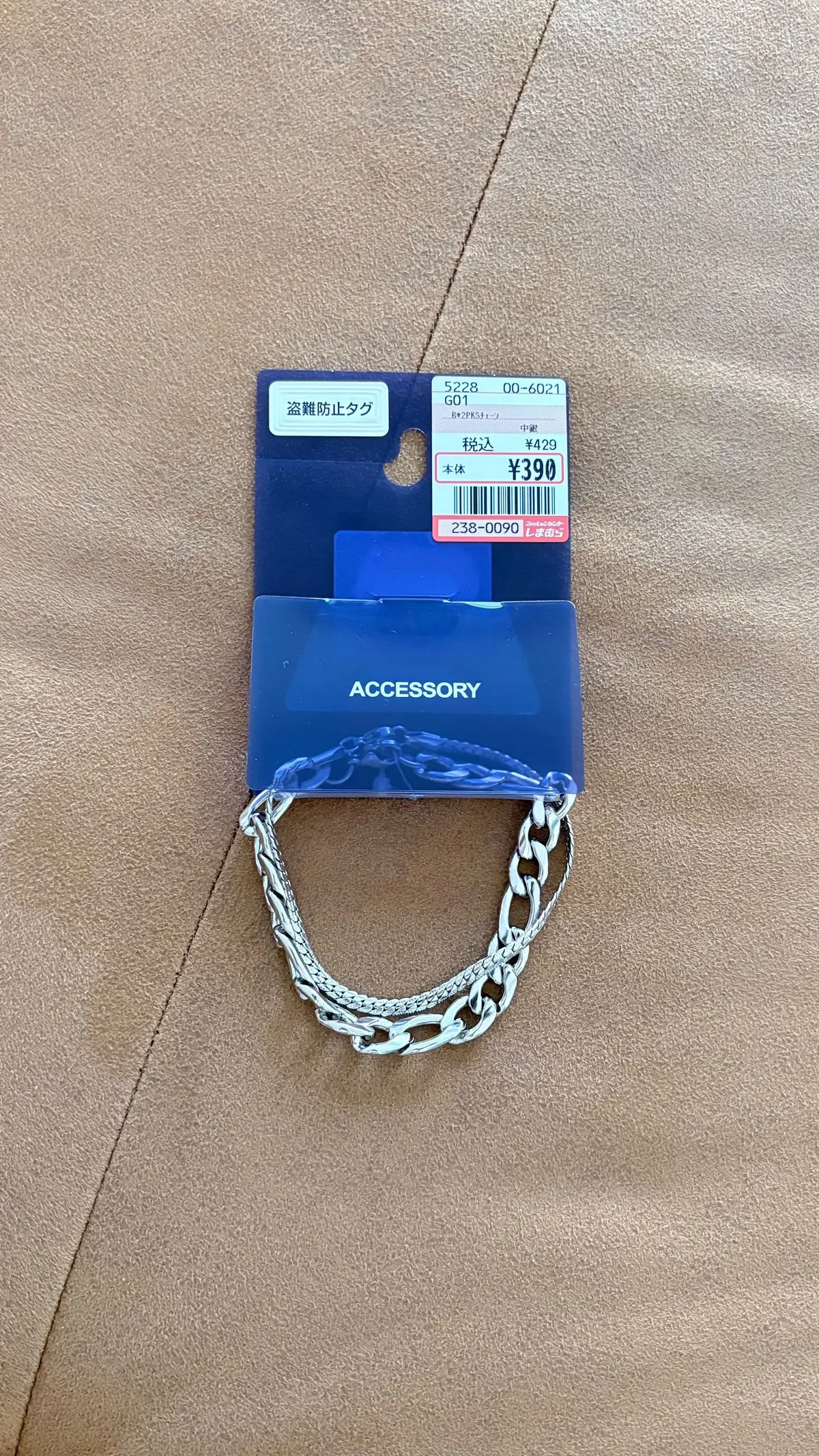 青いアクセサリーの陳列ケースで、チェーン付きの銀色のネックレスが展示されている。価格タグには390円と記載されている。