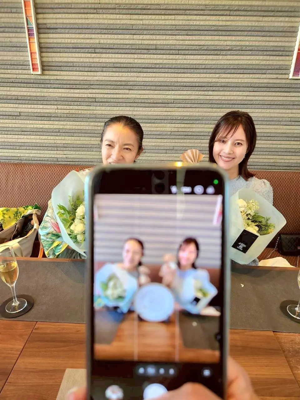 二人の女性が花束を持ってカメラに向かって笑い、スマホでセルフ写真を撮っている